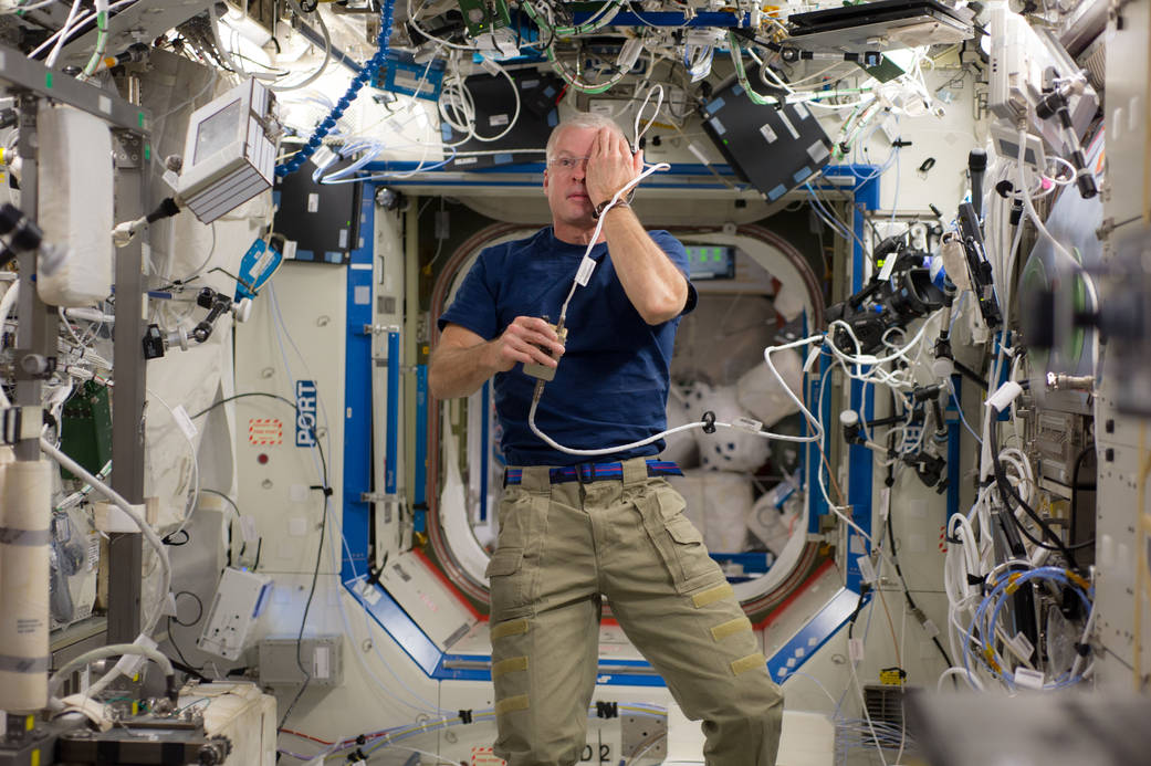 an astronaut floating in the space shuttle with his hand over his eye